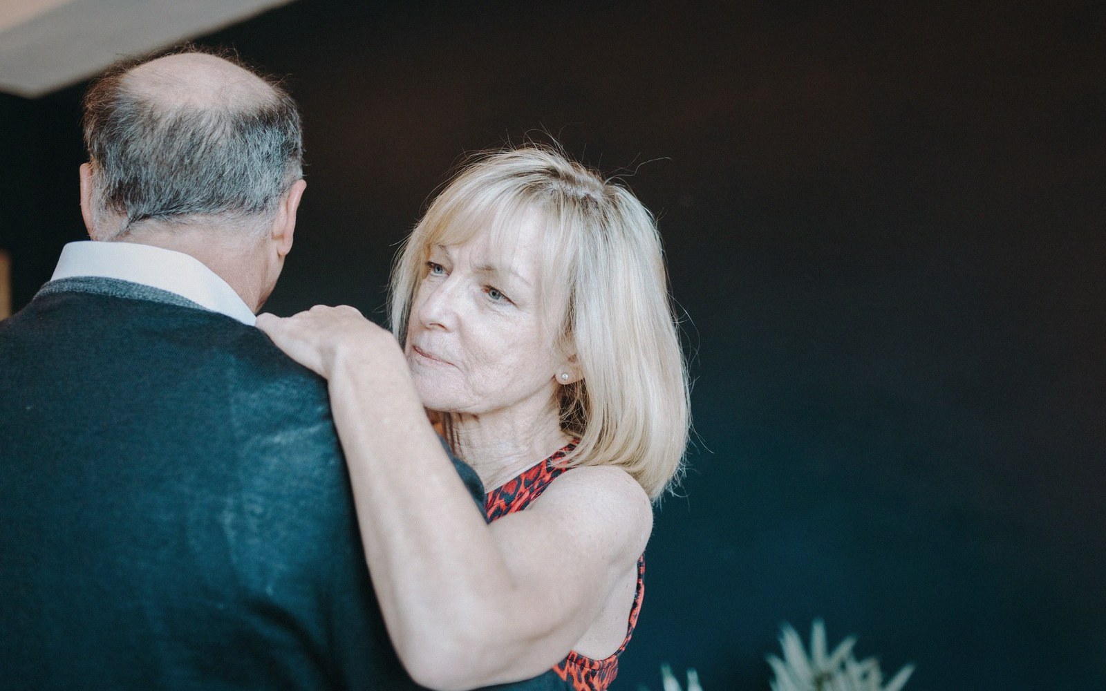An older woman rests her hand on a man's shoulder while dancing closely with him