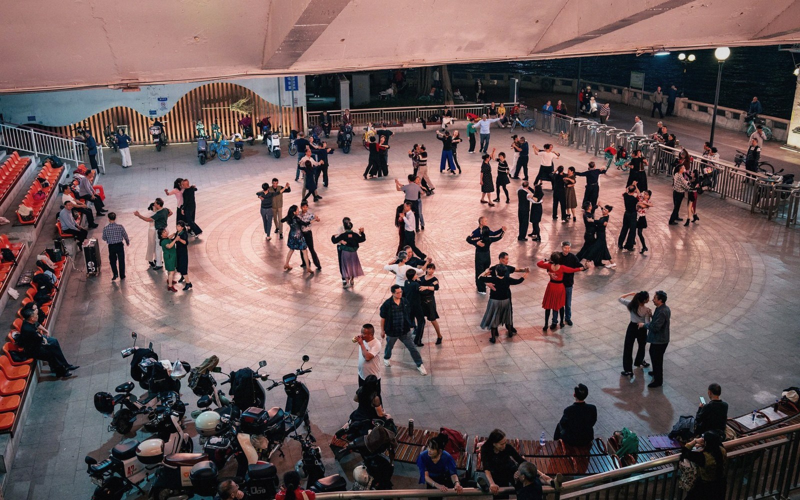 Couples dance in circular patterns on an outdoor plaza dance floor at night