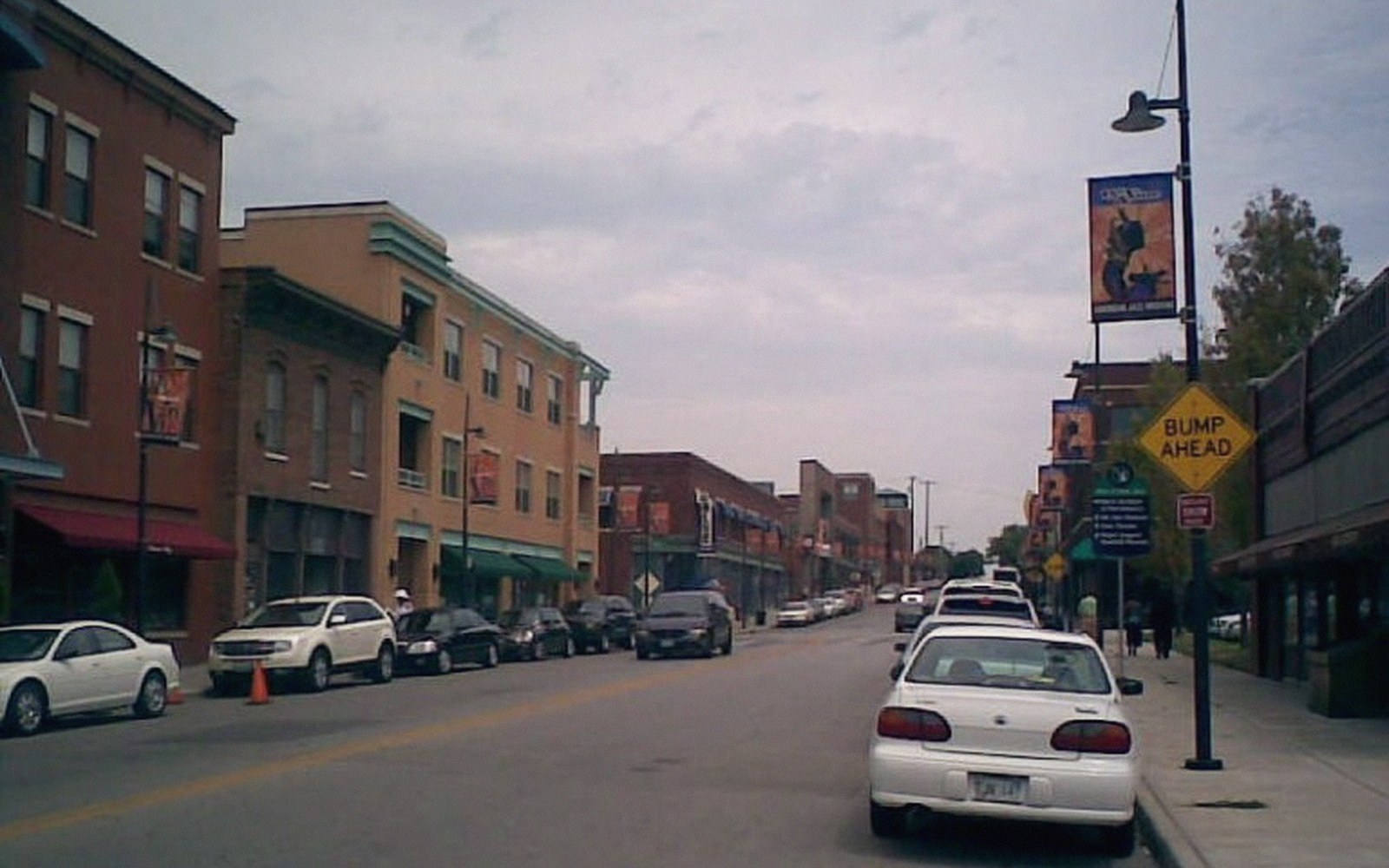 Cars parked along a small-town main street lined with brick storefronts and banners