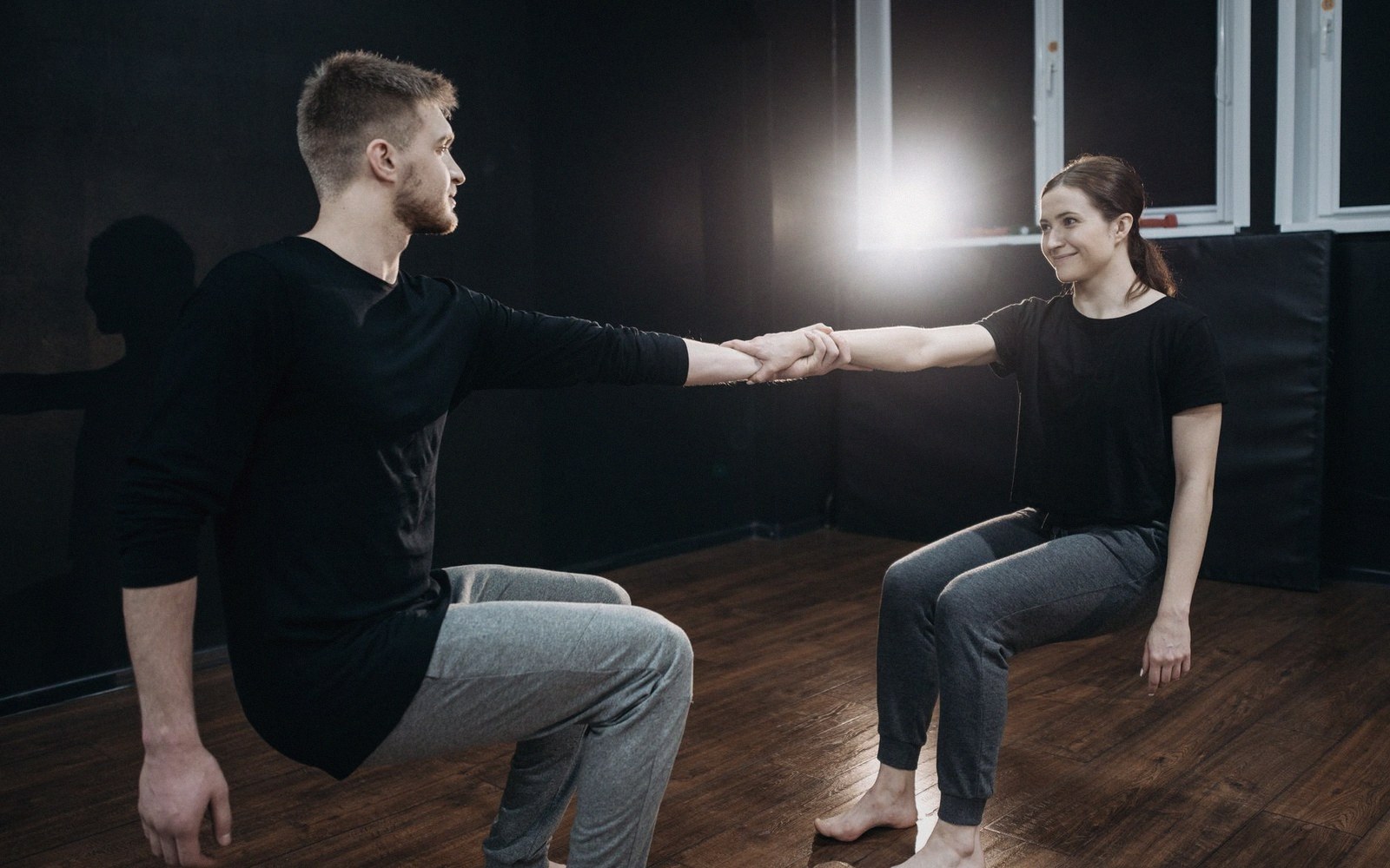 Two dance partners hold hands while balancing in a lunge pose on a wooden floor