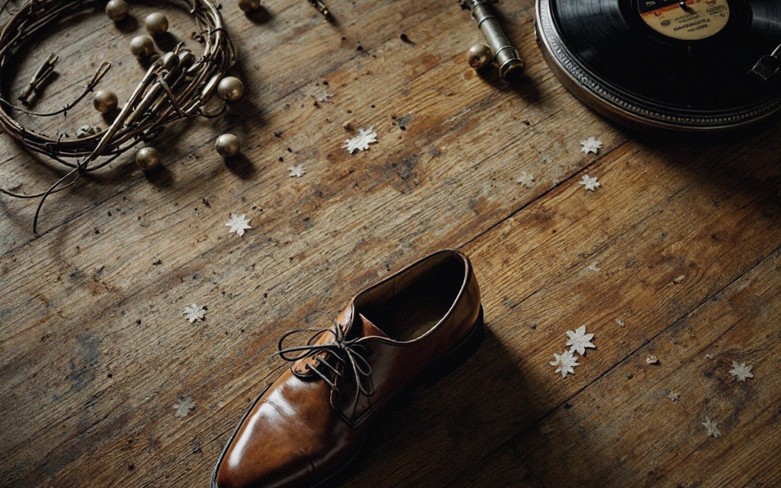 A brown leather oxford shoe on a wooden floor with a vinyl record and beaded wire nearby