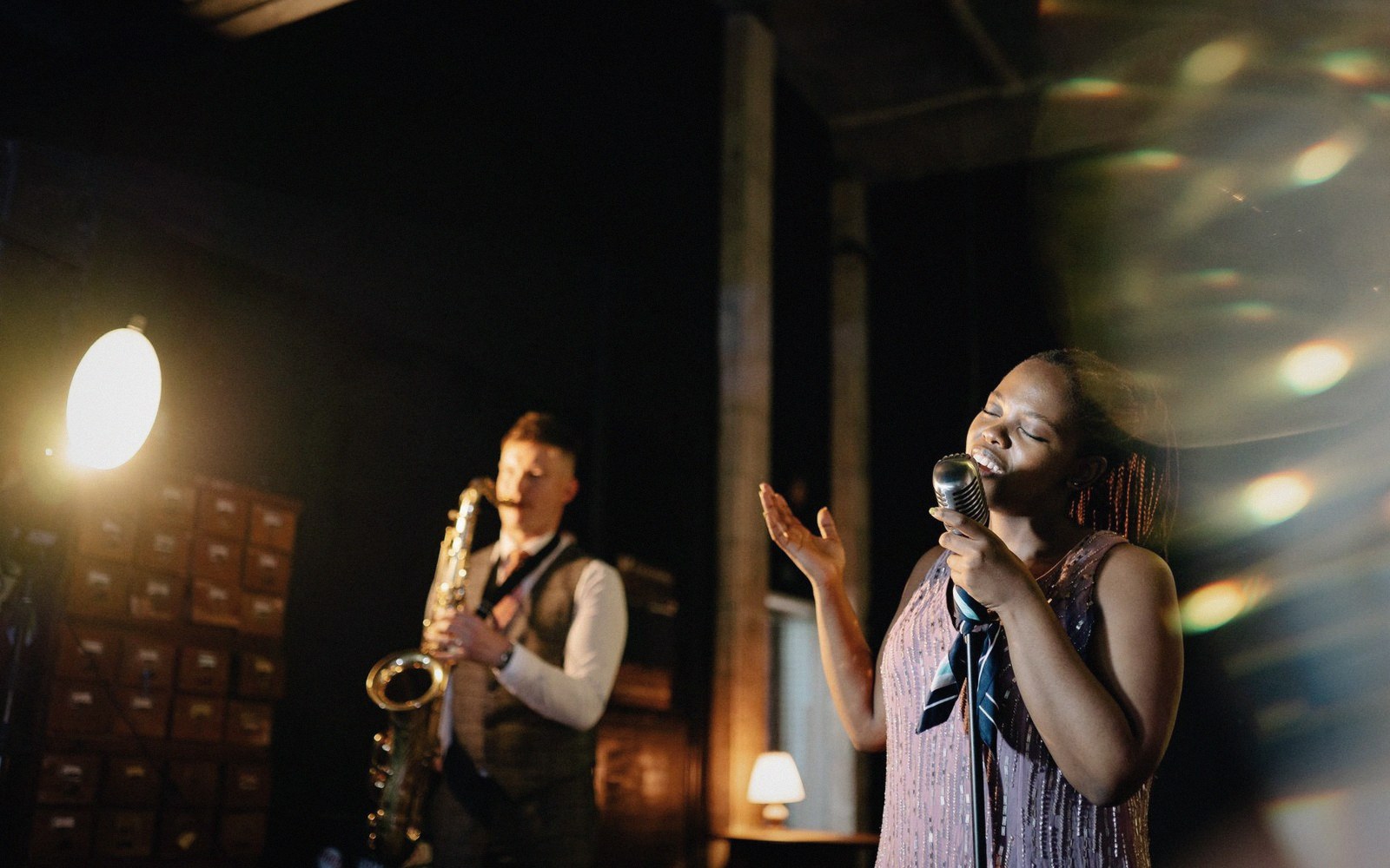 A singer performs into a vintage microphone as a saxophonist plays behind her