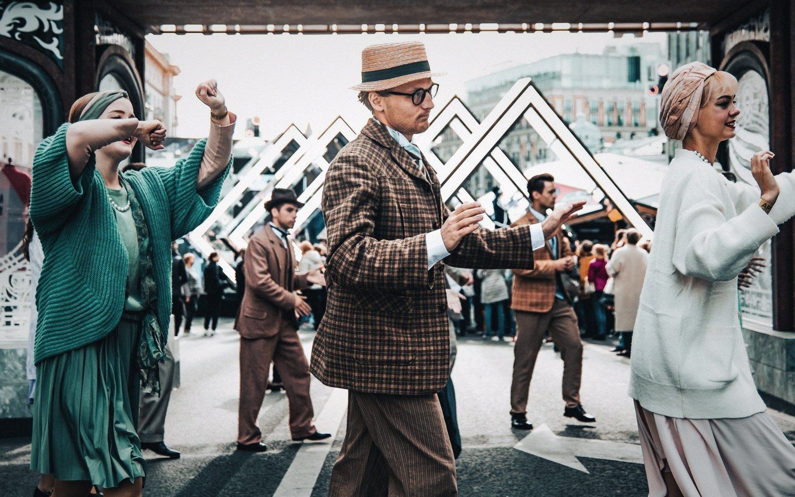 People in vintage-style tweed suits and dresses dance together on a city street